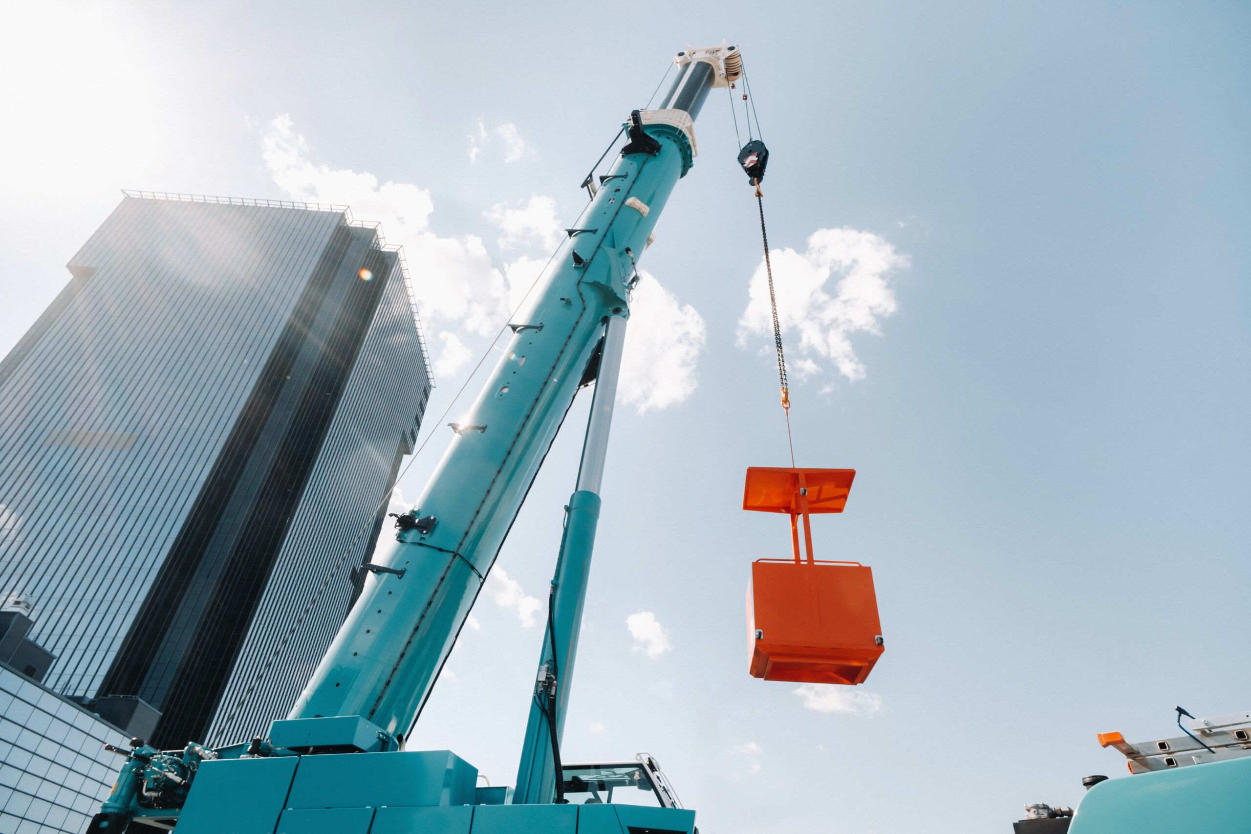 A large blue truck crane stands ready for operation on a site near a large modern building. The largest truck crane with a yellow cradle for solving complex tasks